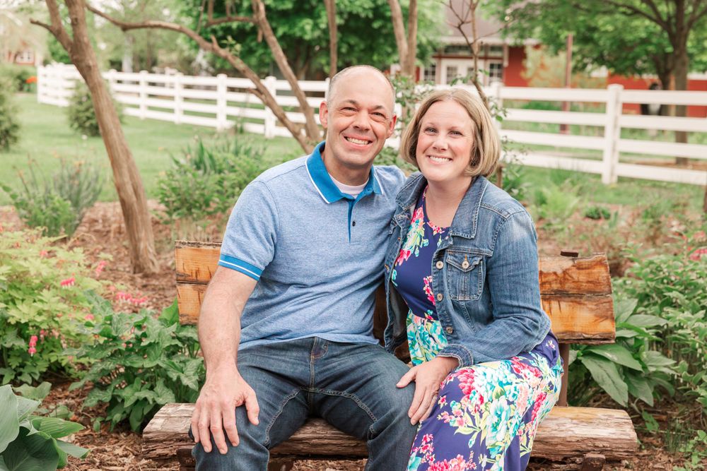 Couple sitting on rustic wooden bench in garden setting.