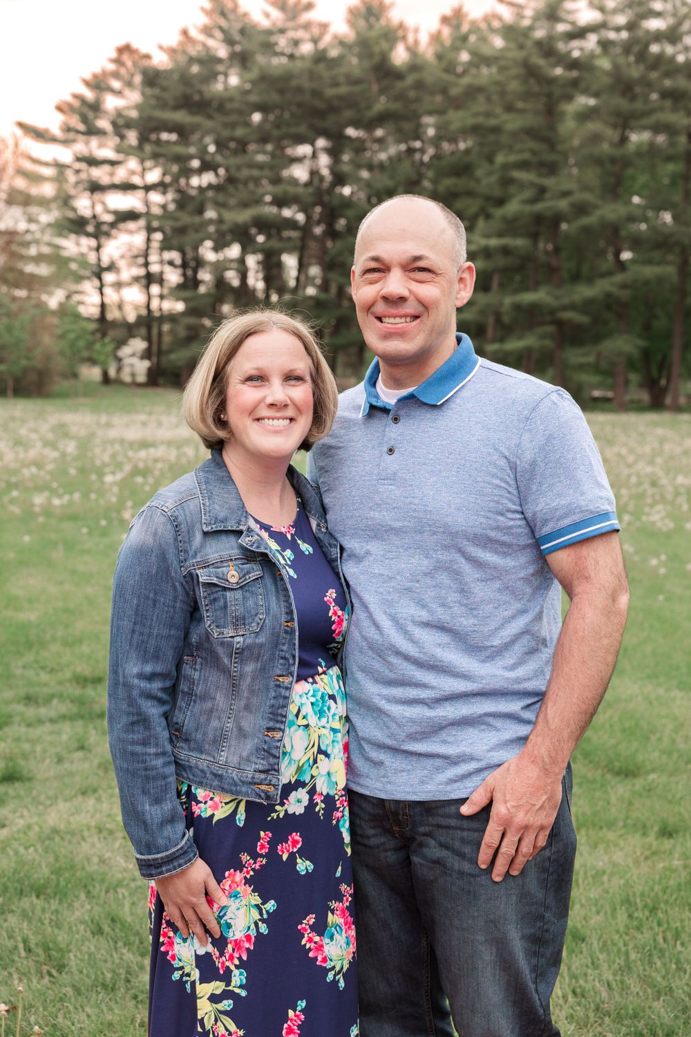 Couple in casual attire posing outdoors with pine forest background.