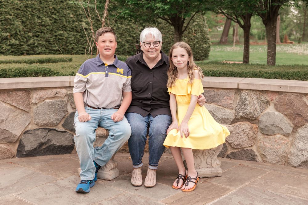 Three people sitting on stone bench in landscaped garden setting.