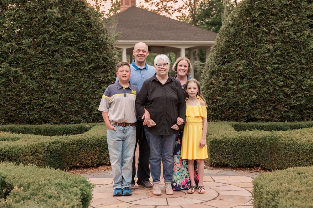 Family portrait taken on stone path surrounded by shaped evergreen hedges and gardens.