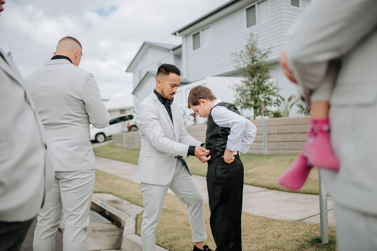 Groomsmen help adjust formal attire during outdoor wedding preparations.