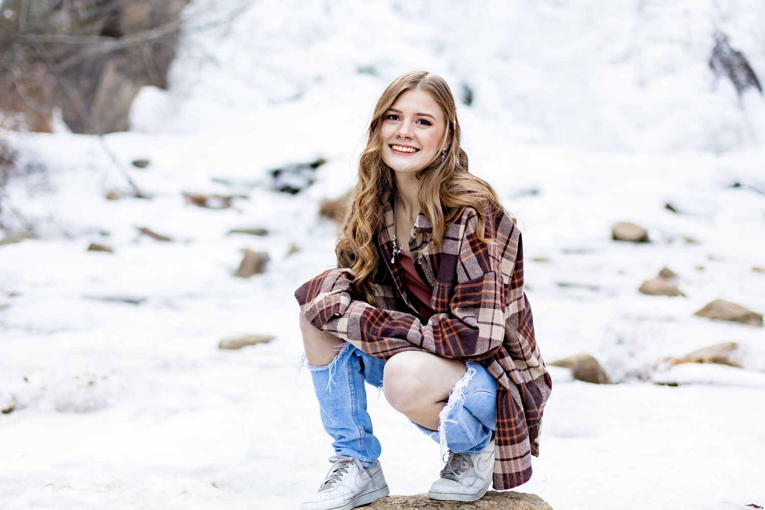 Senior girl squats on the ice and smiles at Helen Hunt Falls in Colorado Springs, Colorado.