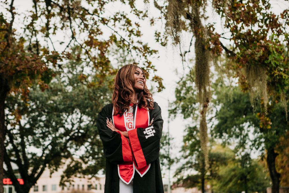 Athletic figure in red and black workout gear poses under moss-draped trees at sunset in an outdoor setting.