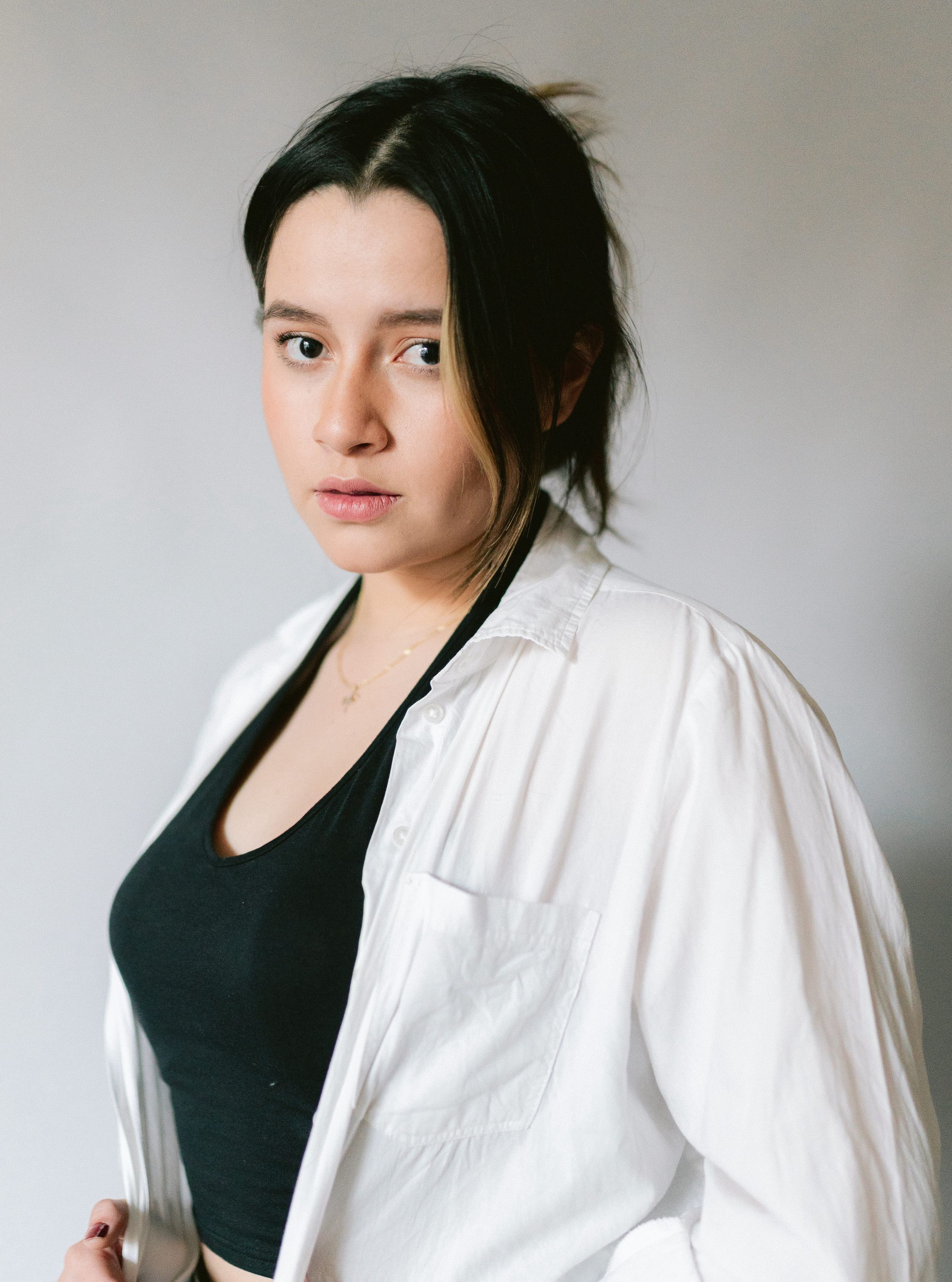 Studio portrait in white button-down shirt and black top against neutral background.