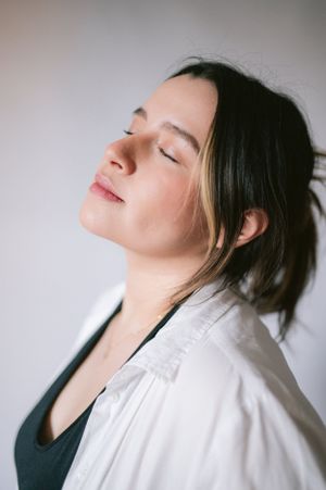 Serene profile portrait with closed eyes wearing white shirt against light background.