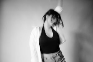 Black and white motion shot of person in black crop top and white jacket with hair in movement.
