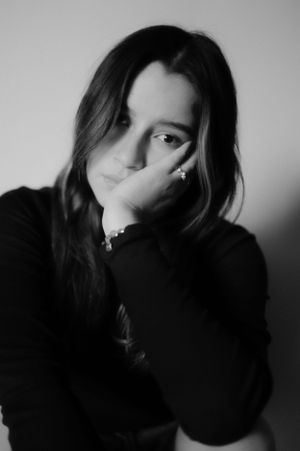 Moody black and white portrait of person with long dark hair resting face on hand.