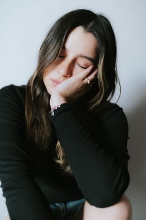 Artistic portrait of person in black sweater with eyes closed resting on hand.
