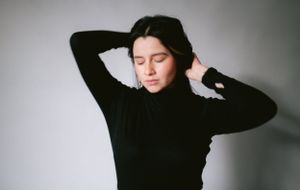 Black and white photo of person in turtleneck with hands in hair against light background.