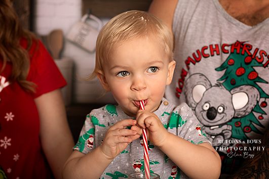 Young child in festive holiday attire enjoying a candy cane treat.