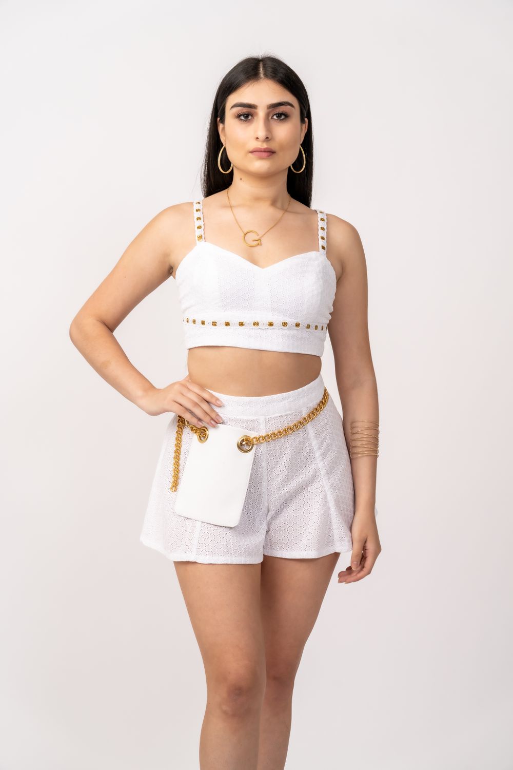 White two-piece outfit featuring studded crop top and shorts with gold chain accessory.