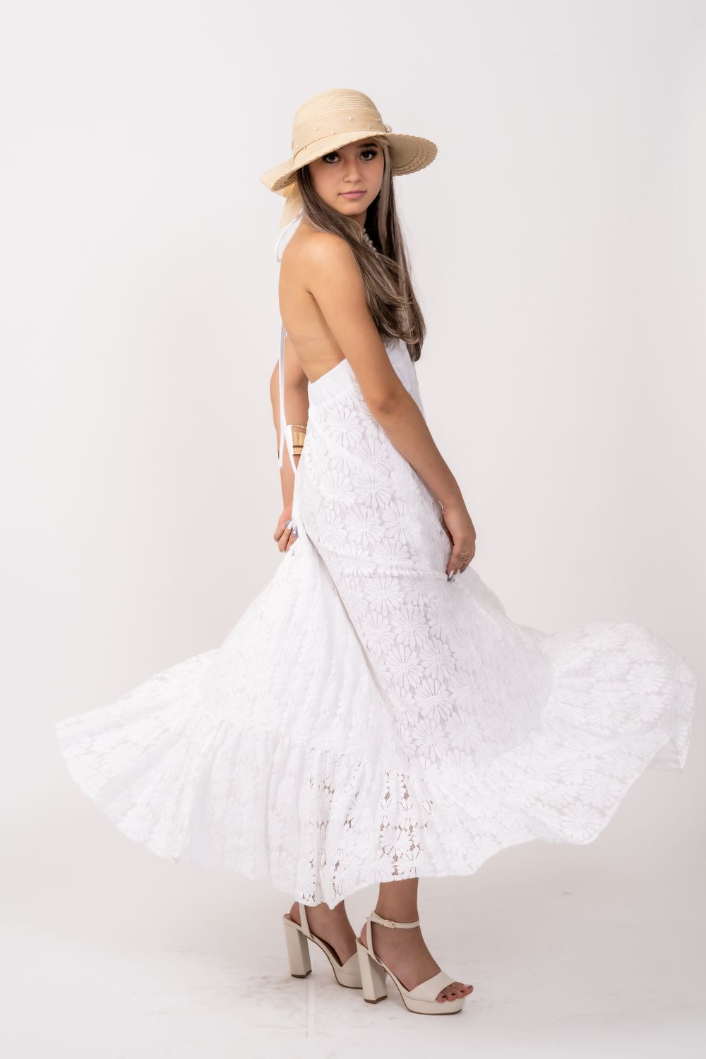 Model in white lace dress and straw hat twirls elegantly against white backdrop.