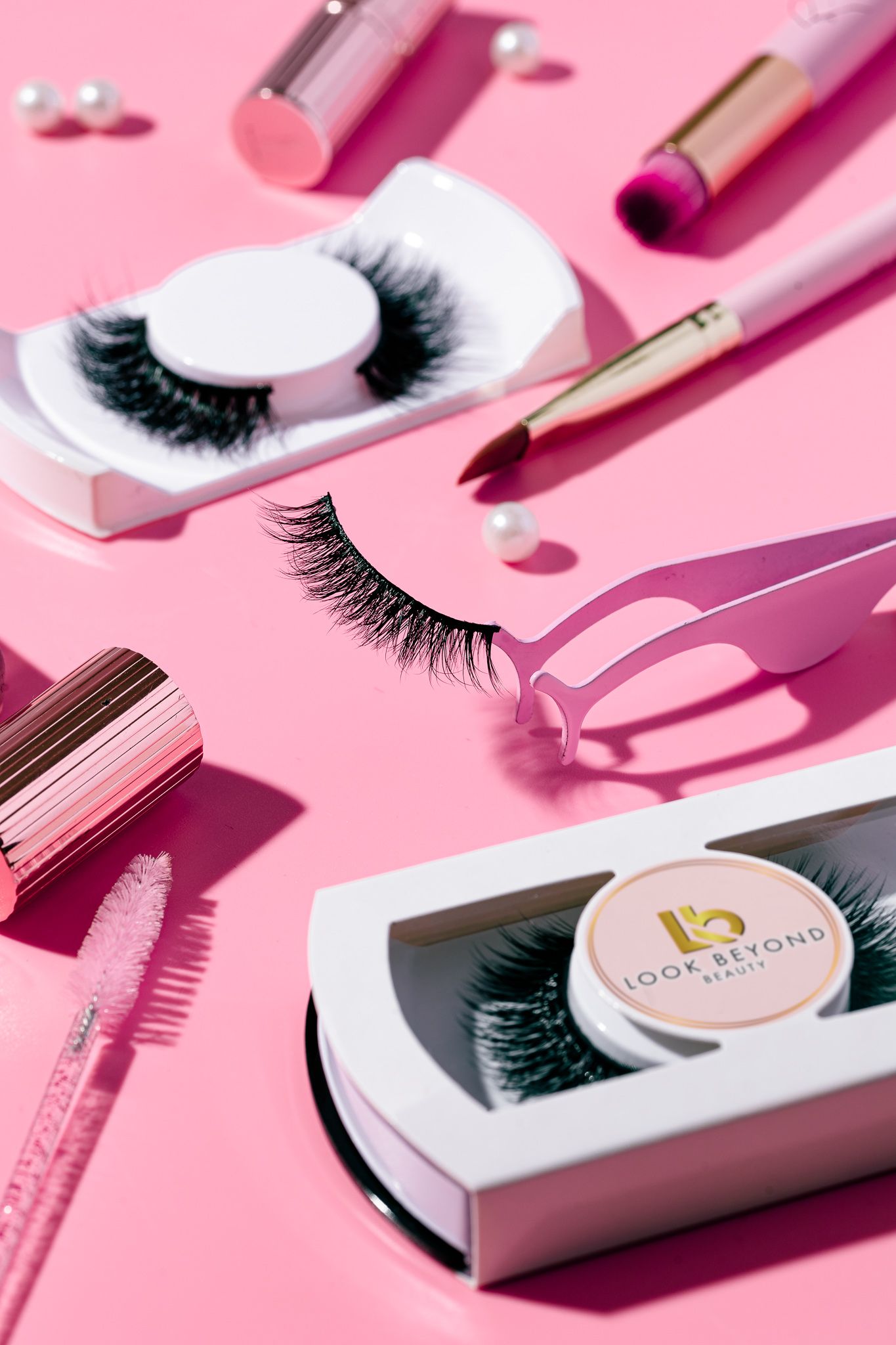 False eyelashes, lipstick and beauty accessories on a pink background for Look Beyond Beauty, cosmetics product photography