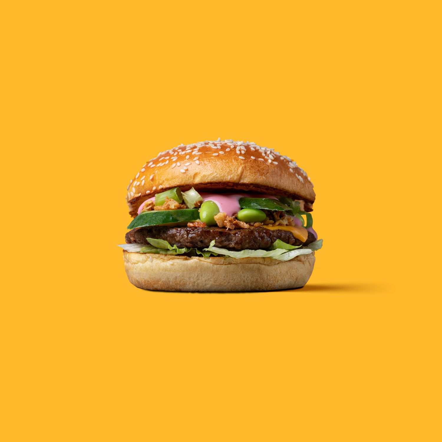 Gourmet burger with lettuce on a bright yellow background, clean studio food product photography Southampton