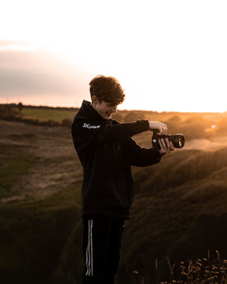 A silhouette of a photographer adjusting camera settings against a golden sunset.