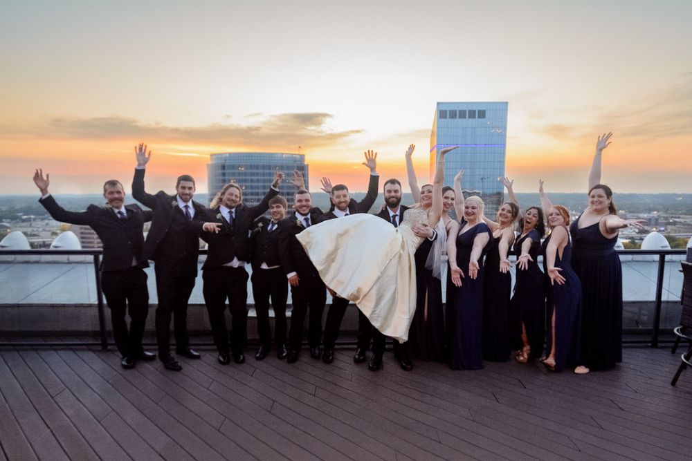 Wedding party celebrating on a rooftop venue at sunset with the bridal couple held aloft.
