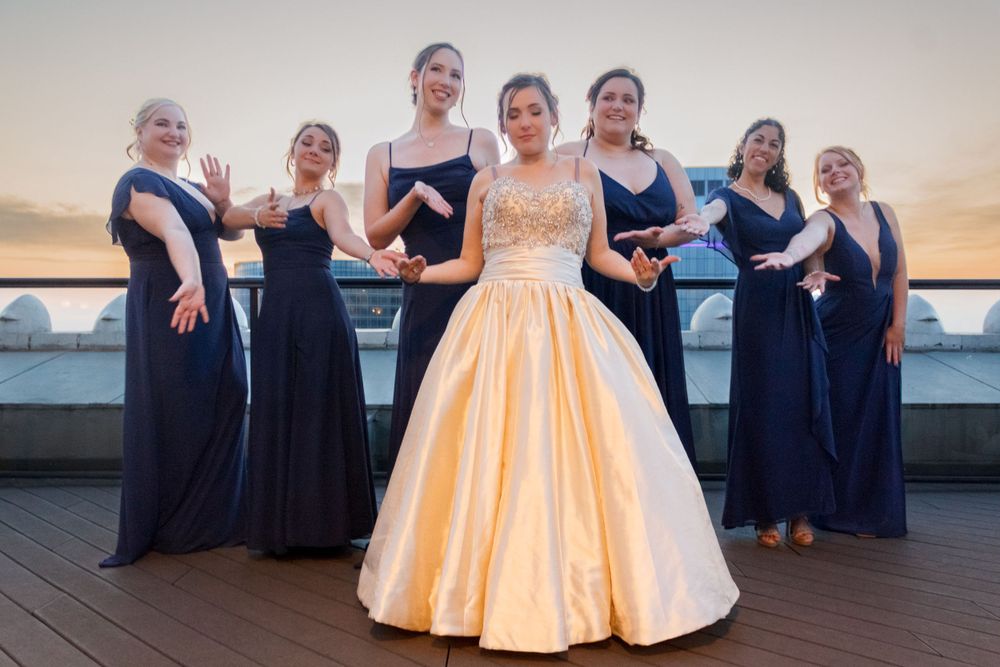 Bridesmaids in navy dresses pose with bride wearing a champagne ball gown on rooftop venue.