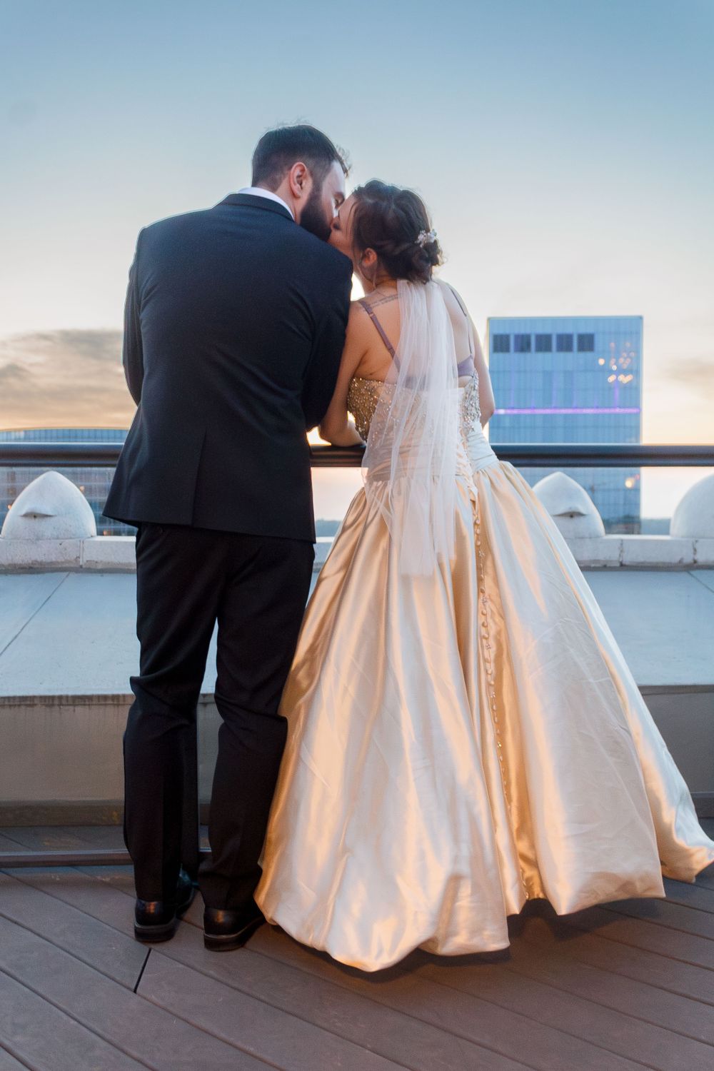 A wedding couple shares an intimate moment on a rooftop terrace at sunset.