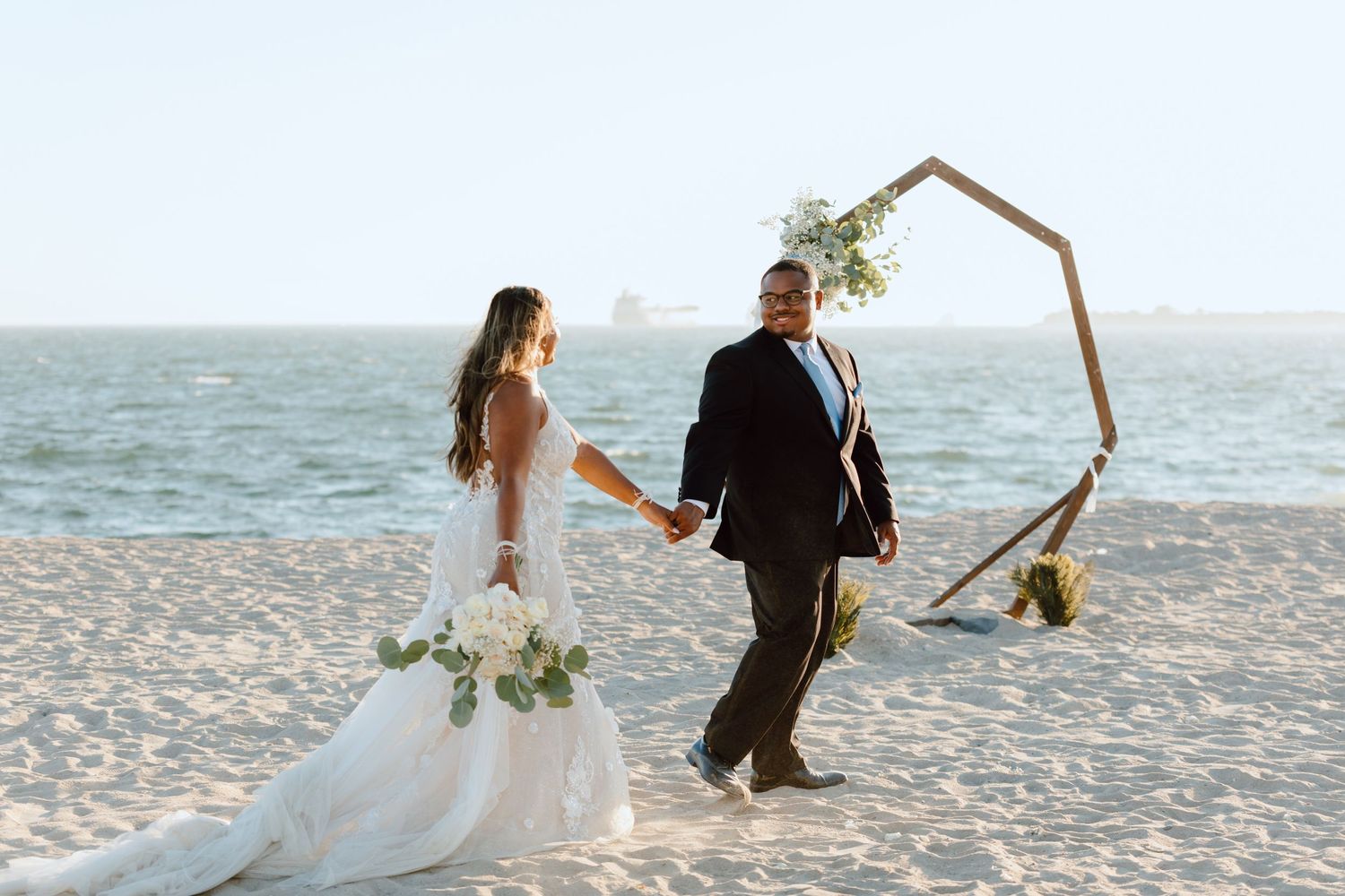 Bridal portraits of a just-married couple walking hand in hand. The ocean and their alter in the background.
