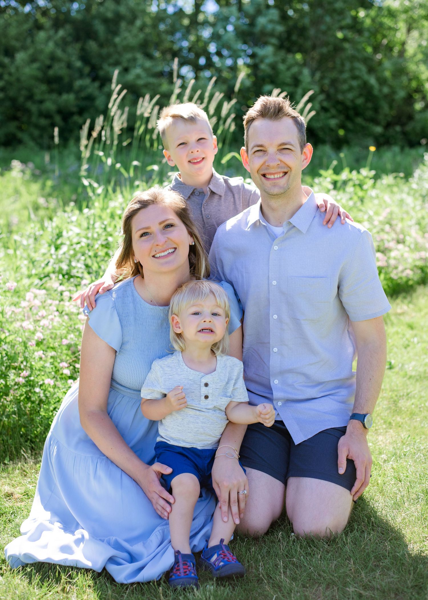 A family of four poses together on grass with wildflowers in the background.