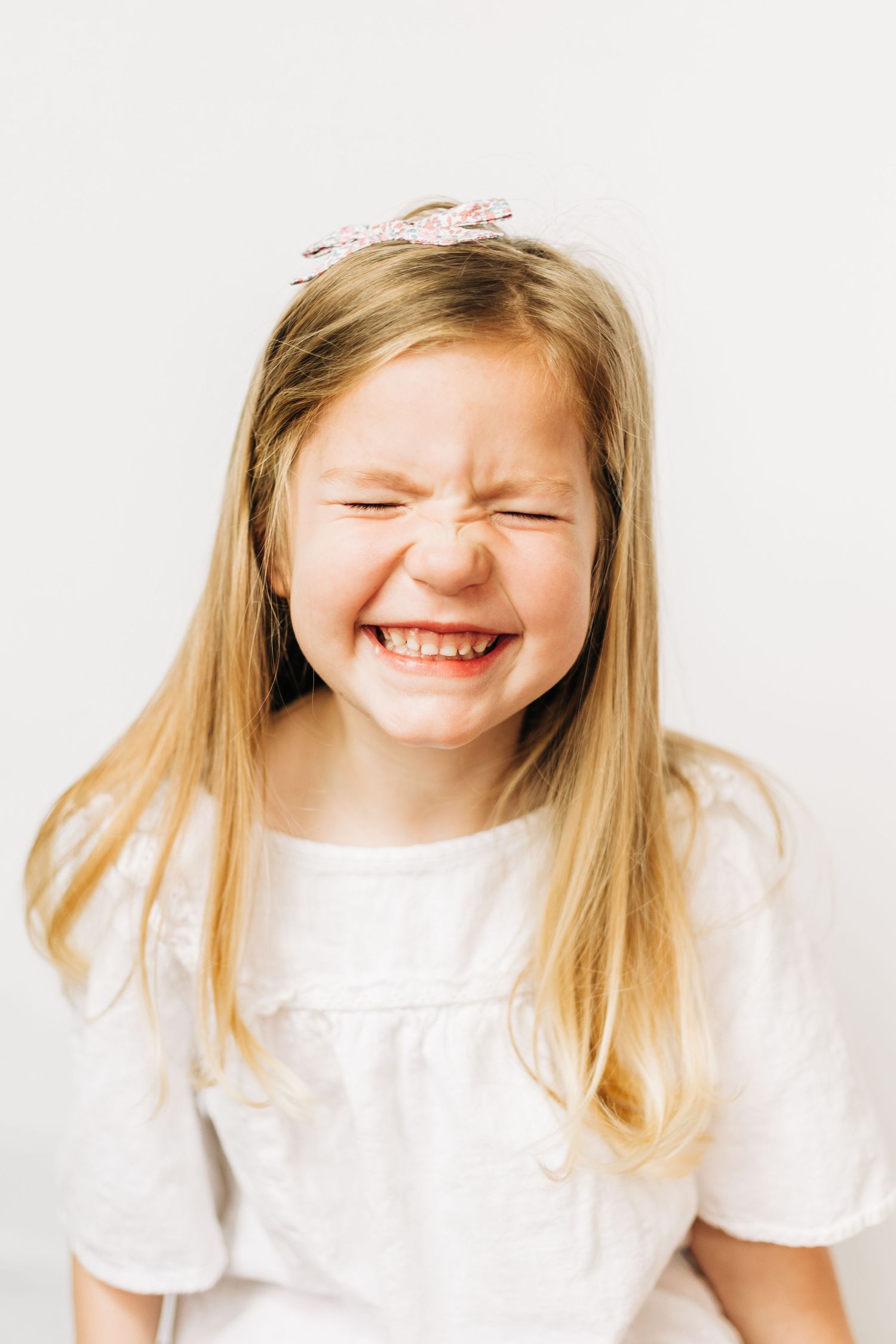 A young child makes a candid expressions showing joyful laughter against a white background.