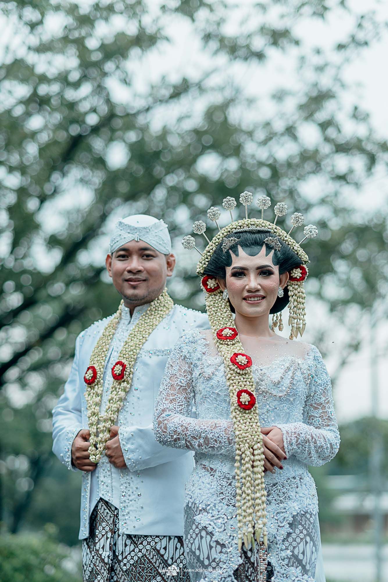 Newlyweds in traditional Javanese wedding attire with ornate headdress and accessories.