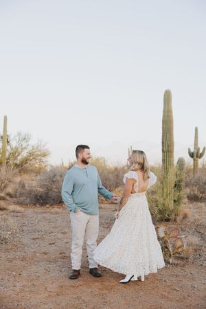 A couple stands together among towering saguaro cacti in the Arizona desert.
