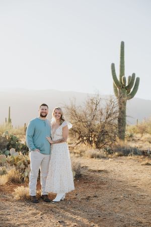 A couple poses for a portrait in front of a majestic saguaro cactus in the desert.