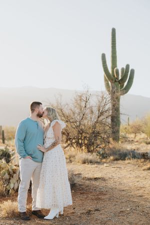 A romantic desert engagement photo with a couple embracing near a tall saguaro cactus.
