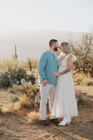 A couple shares an intimate moment in the desert surrounded by cacti and desert flora.