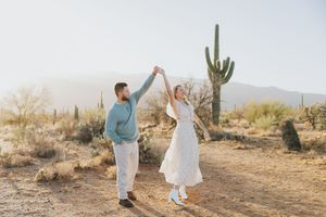 A couple dances together on a desert trail with saguaro cacti in the background.