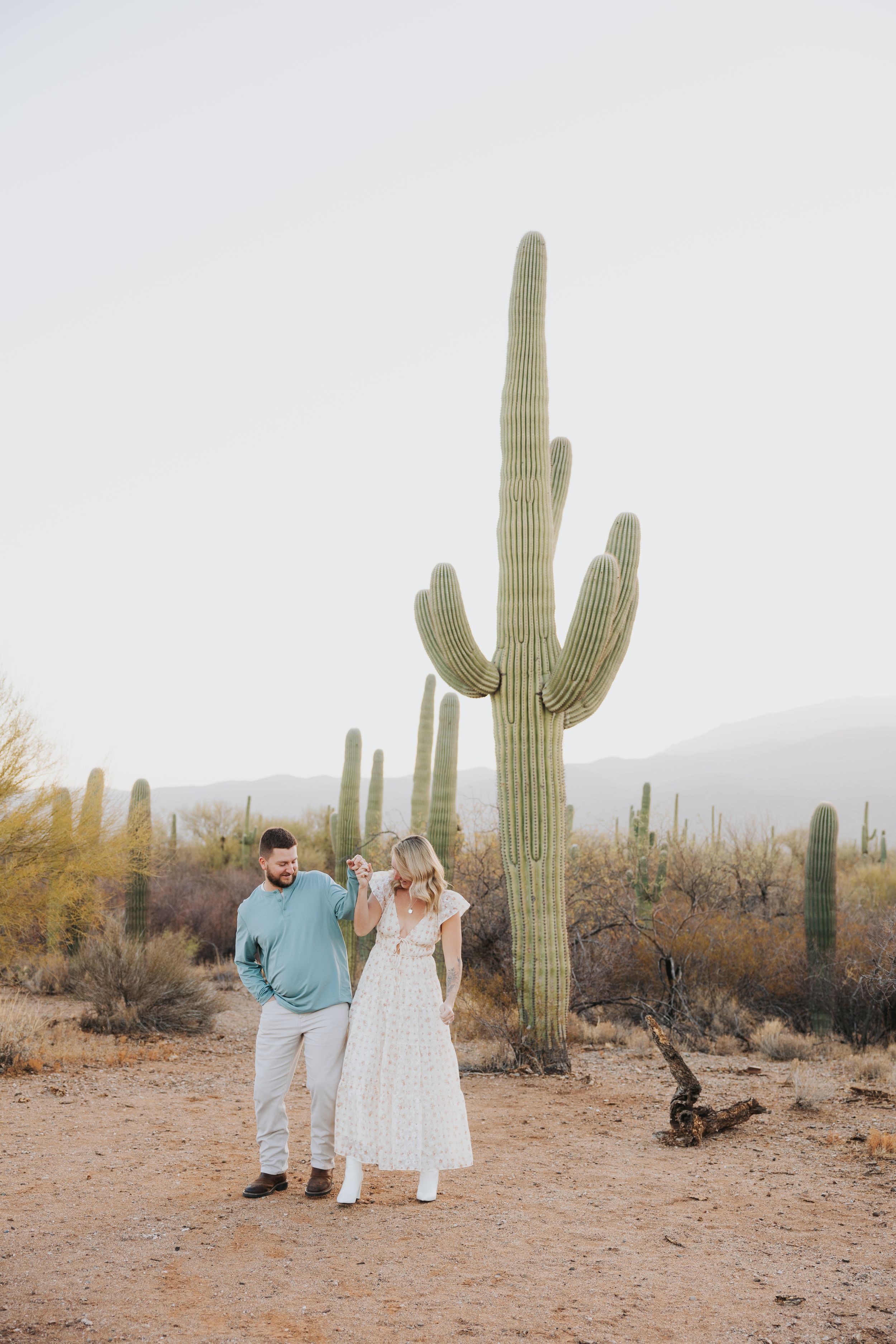 A couple stands beneath a majestic saguaro cactus in the Arizona desert.