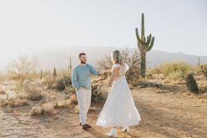 A joyful couple dances in the desert surrounded by majestic saguaro cacti.