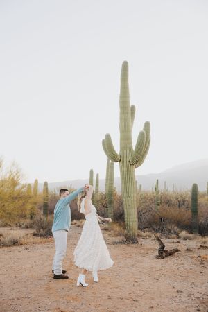A couple dances together in front of a towering saguaro cactus in the desert.