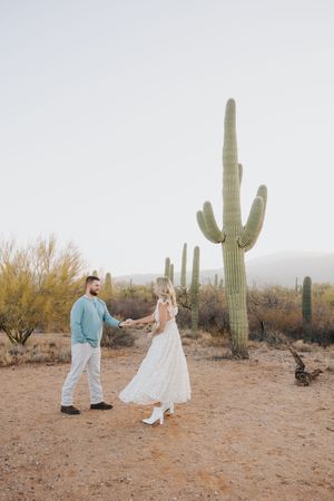 A romantic desert engagement photoshoot with a couple dancing among towering saguaro cacti at sunset.