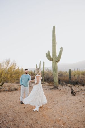Couple in white and turquoise outfits pose for photos in a scenic desert landscape with saguaro cacti.