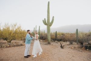 Desert engagement session featuring a couple walking through a field of majestic saguaro cacti.