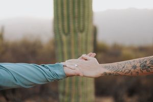 Artistic shot of tattooed hands holding each other against desert backdrop.