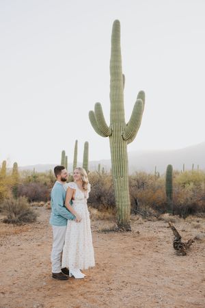 A couple shares an intimate moment in a desert landscape surrounded by tall saguaro cacti.