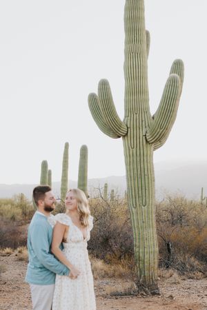 Couple shares romantic moment in front of towering saguaro cactus during desert photoshoot.
