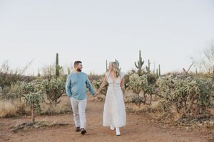 A couple strolls together through a scenic desert path surrounded by cacti.