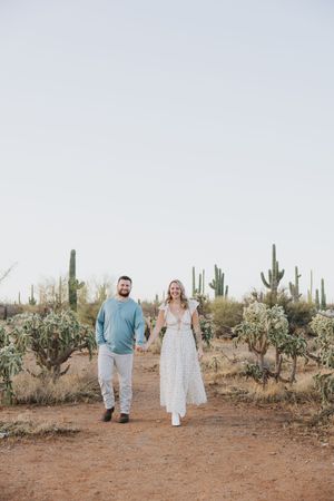 A couple explores a desert trail with majestic saguaro cacti in the background.