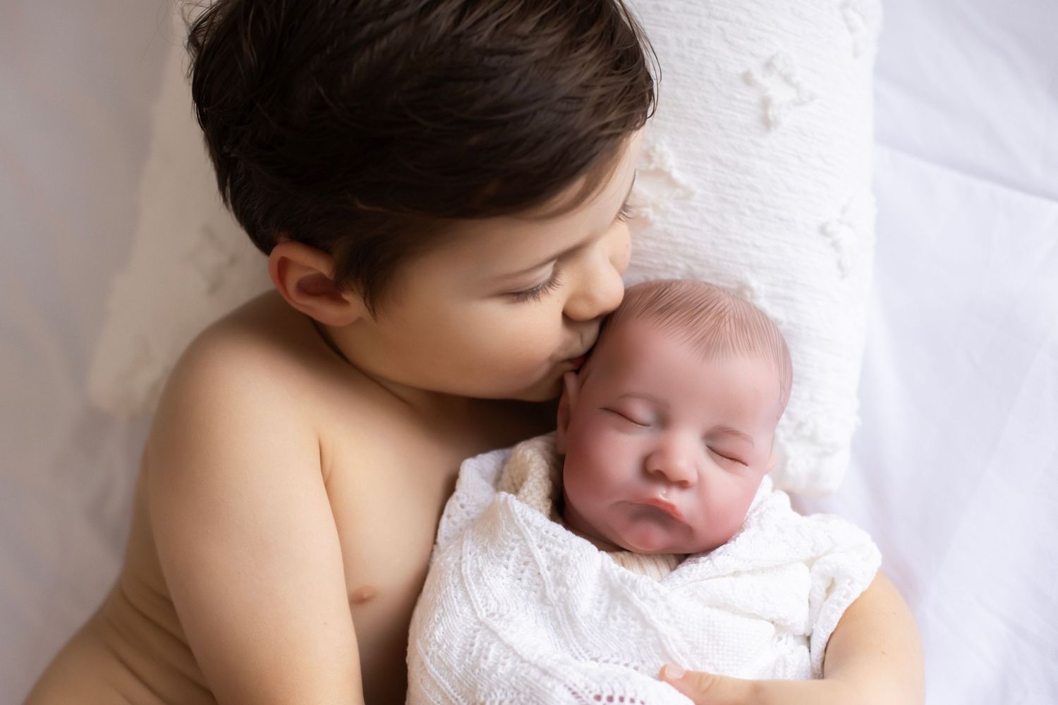 Little boy holding a baby doll, kissing the baby doll's head.