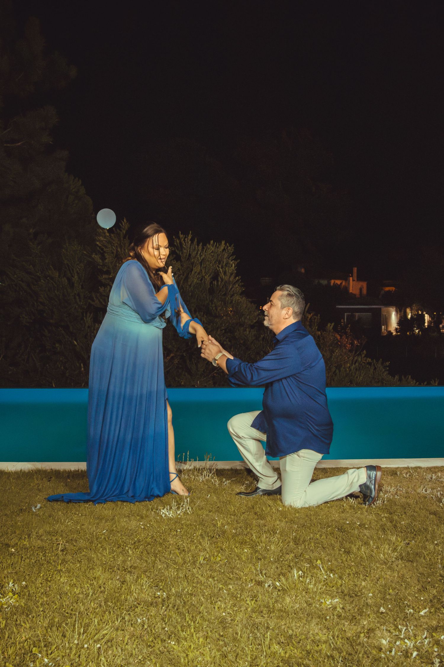 Marriage proposal scene at night with a blue railing and grass in the background.