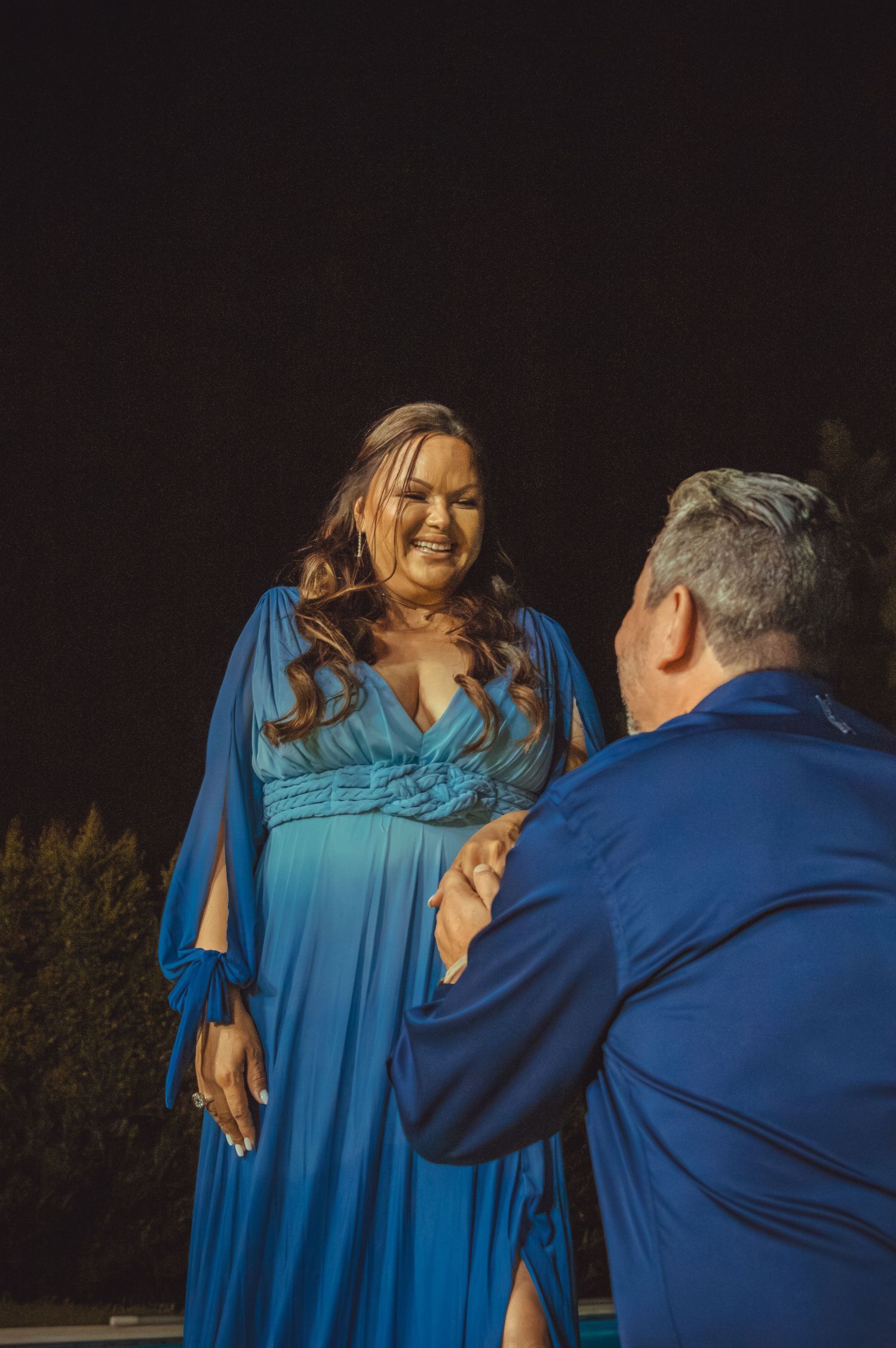 Couple in matching blue outfits sharing an emotional moment during a nighttime proposal.