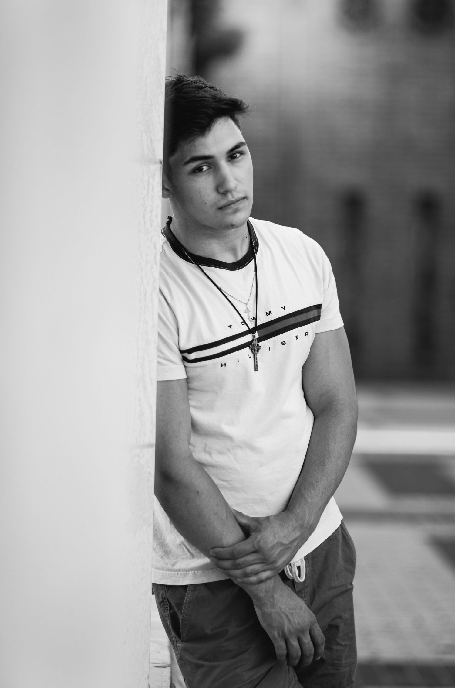 Portrait of young person in white t-shirt leaning against wall in black and white photography.
