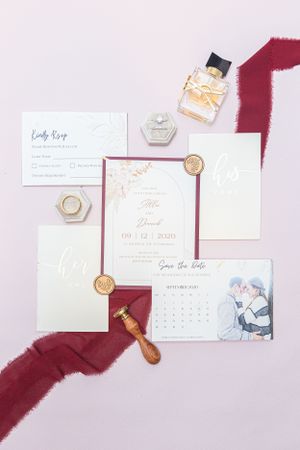 Wedding invitation suite with burgundy accents featuring save the date cards, wax seals, perfume bottle and silk ribbon.