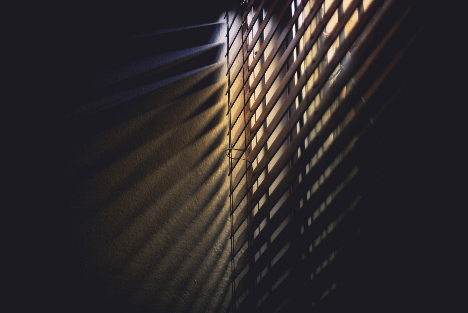 Dramatic light beams streaming through window blinds creating geometric shadows.