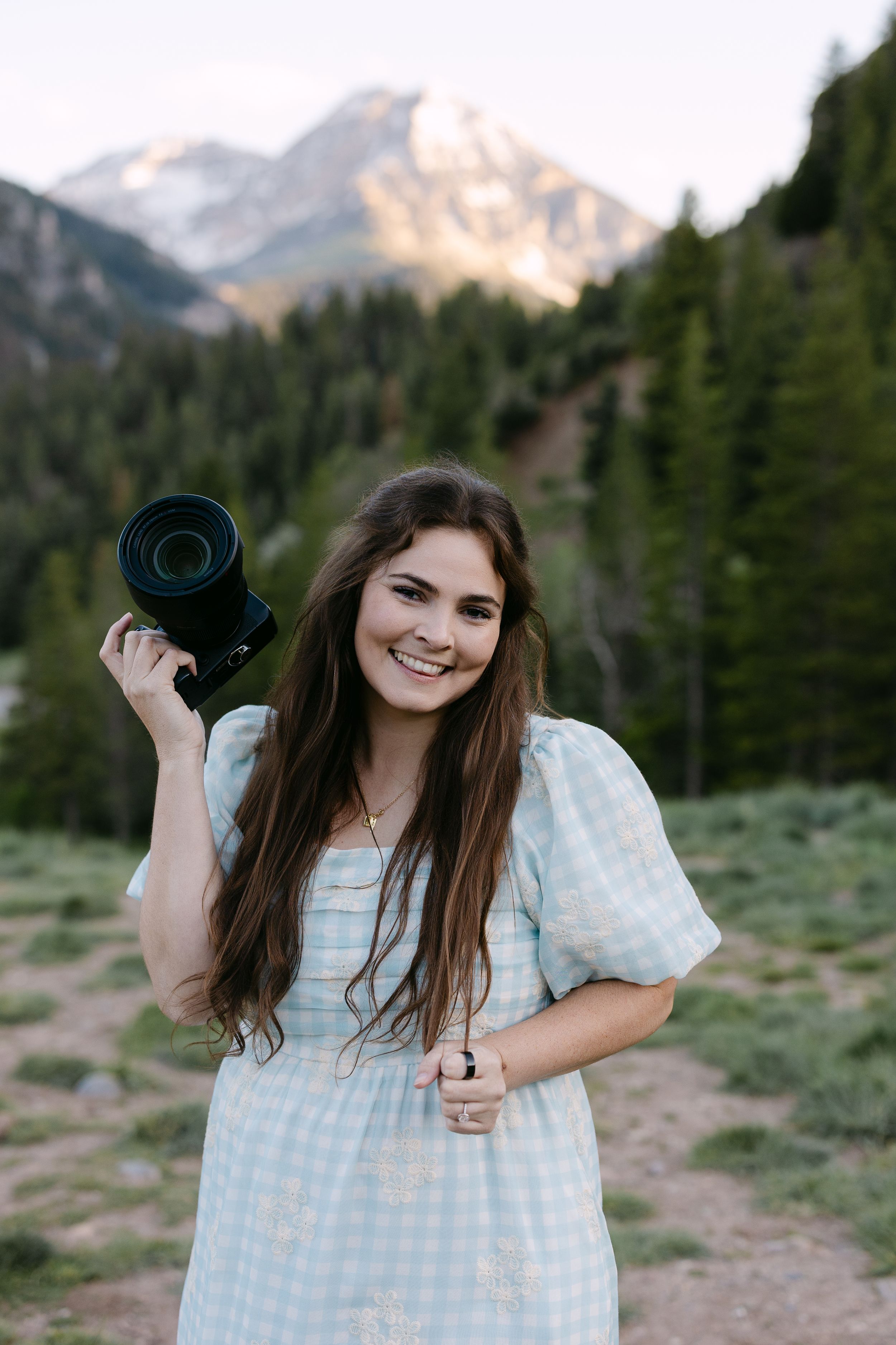 Black and white portrait of someone holding a vintage camera while wearing a knit sweater and smiling.