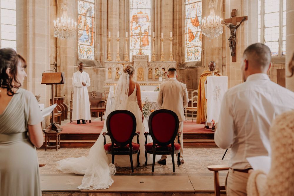 A traditional church wedding ceremony in progress with ornate stained glass windows and red velvet chairs at the altar.